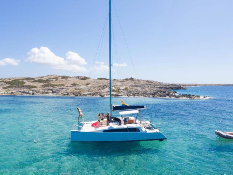 group of friends on the day trip ibiza catamaran aventura 28 jumping into the water and having fun in the bow of the boat