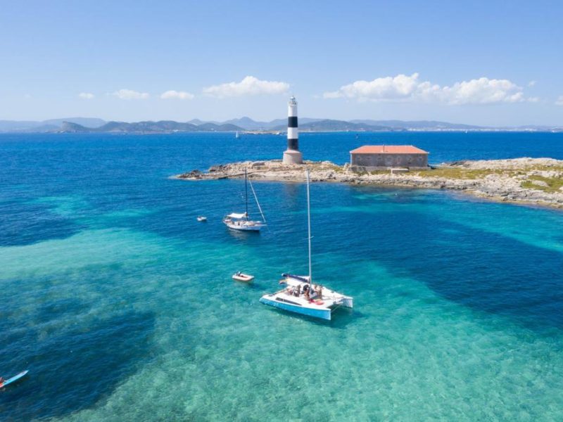 bird´s view of the catamaran aventura 28 anchored in espalmador island with the blue turquoise water and the dark Posidonia next to the boat